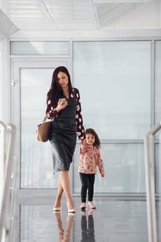 Young mother with her daughter walking together indoors in the office or airport. Having vacation.