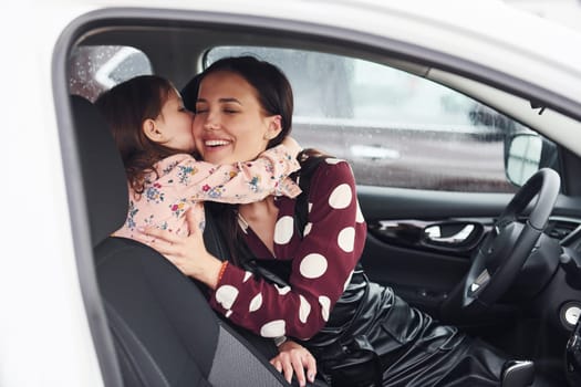 Embracing each other. Mother with her daughter inside of modern automobile together.