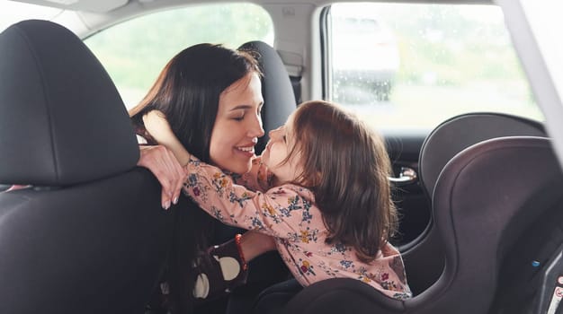 Embracing each other. Mother with her daughter inside of modern automobile together.