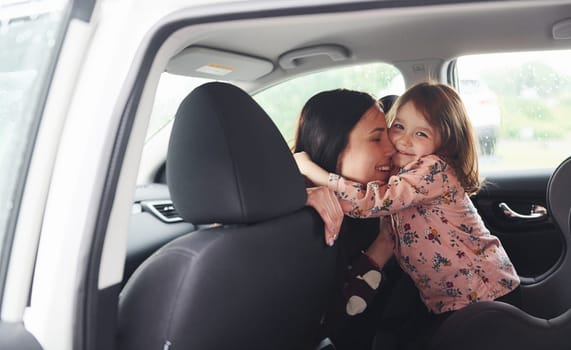 Embracing each other. Mother with her daughter inside of modern automobile together.