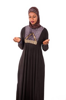 young muslim woman standing in long dress looking down with open palms.