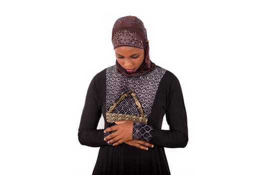 young muslim woman standing in long dress looking down hands crossed.