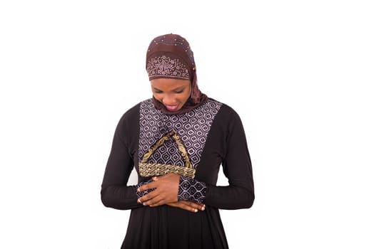 young muslim woman standing in long dress looking down hands crossed smiling.