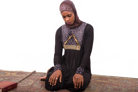 young muslim woman sitting in long dress on mat praying.