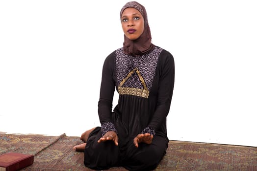 young muslim woman sitting in long dress on mat praying.