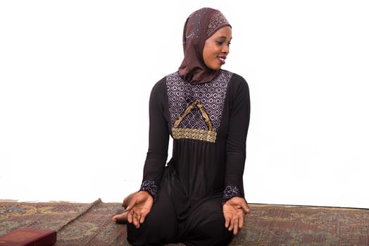 young muslim woman sitting in long dress on mat praying looking at profile smiling.