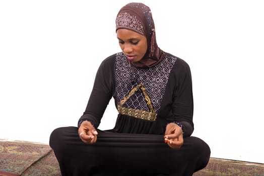 young muslim woman sitting on a mat praying.