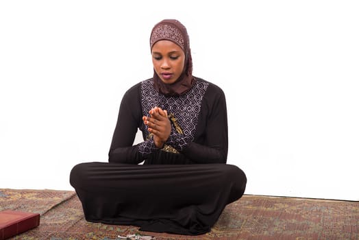 young muslim woman sitting on a mat praying.