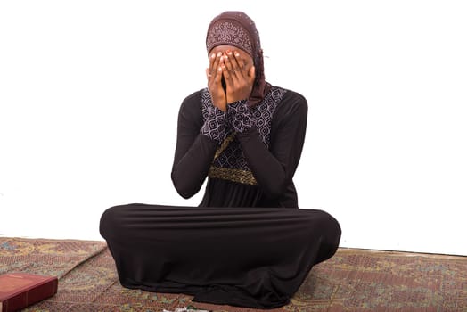 young muslim woman sitting on a mat praying.