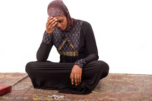young muslim woman sitting on a mat praying with a smile.