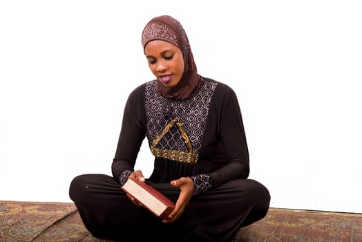 young muslim woman sitting on a mat watching the koran smiling.