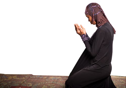 young muslim woman kneeling on a mat praying.