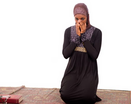 young muslim woman kneeling on a mat praying.