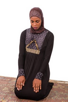 young muslim woman kneeling on mat praying.