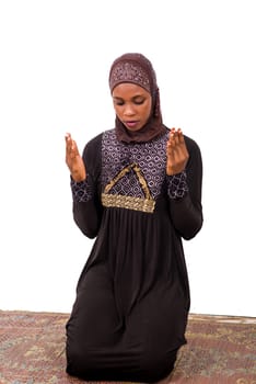 young muslim woman kneeling on mat praying.