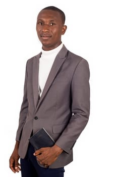 young smiling pastor standing in jacket and holding a Bible on white background.