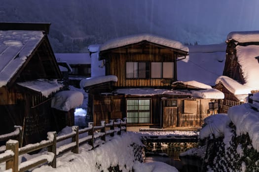 Heavy snow falls on traditional wooden homes in Japanese village at night. High quality photo