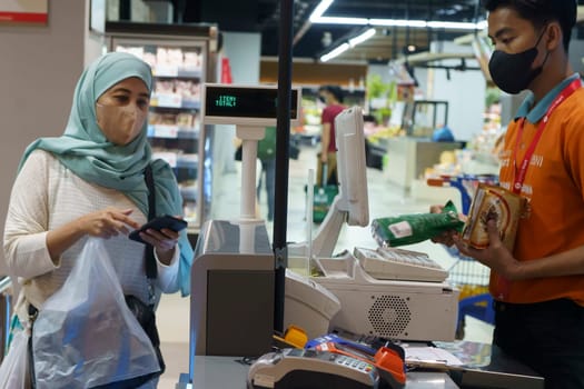 March 25, 2023. Muslim woman paying her shopping with her smartphone in grocery store in Surabaya, Indonesia in Ramadhan 2023.