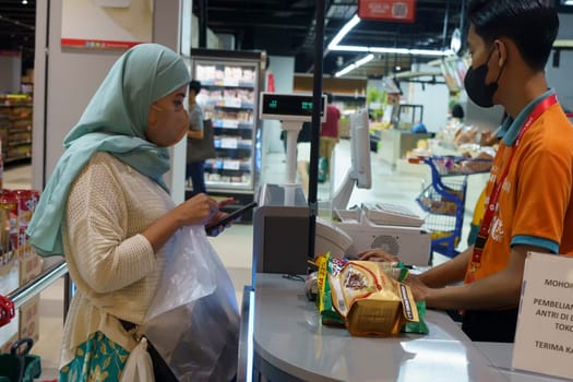 March 25, 2023. Muslim woman paying her shopping with her smartphone in grocery store in Surabaya, Indonesia in Ramadhan 2023.