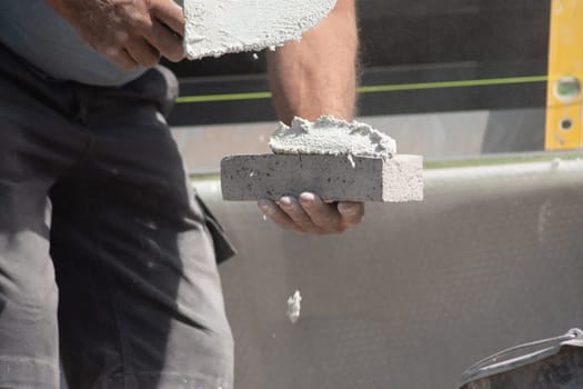 close up of the hands of a bricklayer applying cement mortar to a brick to stick it into the masonry for building a house, High quality photo
