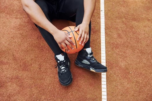 Tired african american man sits on the ground with ball on the court outdoors. Takes a break.