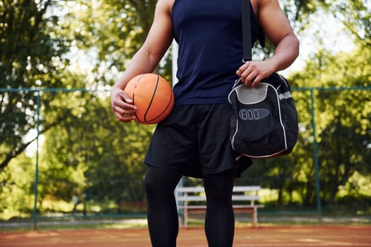 Beautiful green trees on background. African american man plays basketball on the court outdoors.