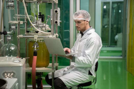 Apothecary scientist using laptop to record information from a CBD oil extractor and a scientific machine used to create medicinal cannabis products.