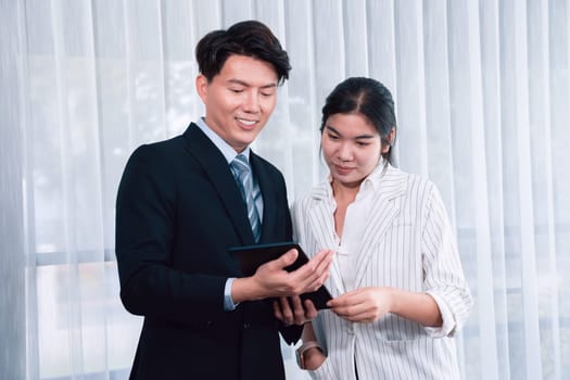 Manager advising guiding younger colleague with tablet in workplace. Couple businesspeople in formal wear working together on financial strategy as concept of teamwork and harmony in office.