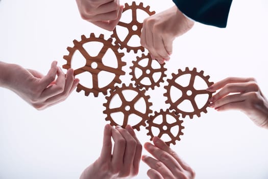 Hand holding wooden gear by businesspeople wearing suit for harmony synergy in office workplace concept. Isolated background. Bottom view of people hand make chain of gear into collective unity symbol