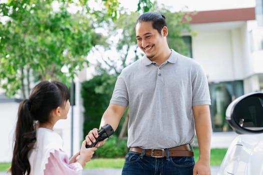 Progressive father and daughter returned from school in electric vehicle that is being charged at home. Electric vehicle driven by renewable clean energy. Home charging station concept for environment