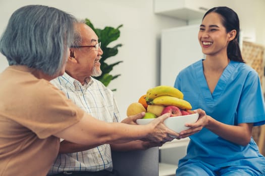 Contented senior couple taking a bowl of fruit from a nurse at home. Senior care at home.