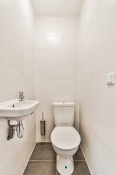 a bathroom with white tiles on the wall and toilet in the corner, there is a sink next to the toilet