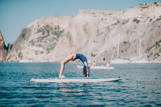 Woman sup yoga. Middle age sporty woman practising yoga pilates on paddle sup surfboard. Female stretching doing workout on sea water. Modern individual hipster outdoor summer sport activity