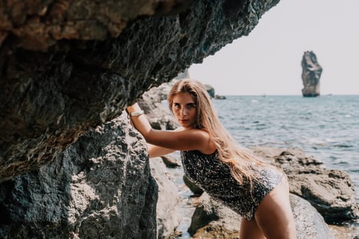 Woman travel sea. Young Happy woman in a long red dress posing on a beach near the sea on background of volcanic rocks, like in Iceland, sharing travel adventure journey