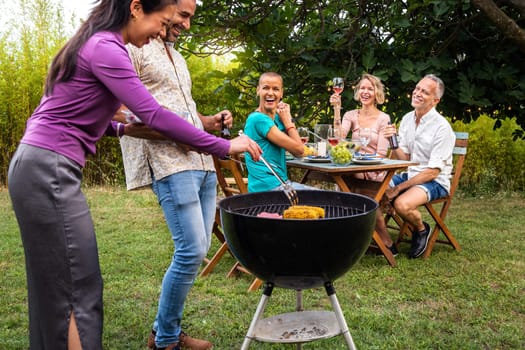 Friends cooking food on grill. Outdoor garden barbecue party. Friends laughing and having fun, enjoying wine in backyard. Friendship concept.