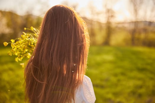 photo from the back of a red-haired woman with a bouquet of flowers in the rays of the setting sun. High quality photo