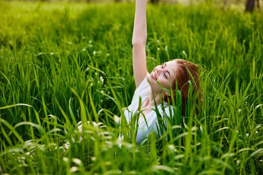 a cute woman in the summer high grass sits in a light dress happily raising her hand up. High quality photo