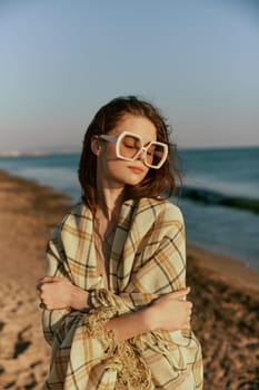 portrait of a woman in massive glasses wrapped in a plaid enjoying a warm day at the sea, facing the camera. High quality photo