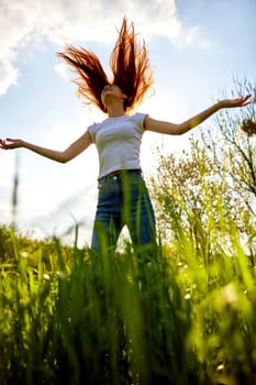 a happy woman in summer clothes stands in a field lit from behind and with her hair flying in the air. High quality photo