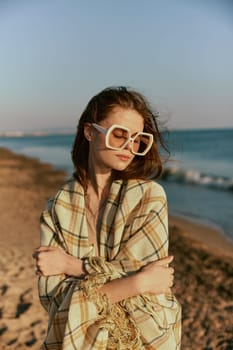 portrait of a woman in massive glasses wrapped in a plaid enjoying a warm day at the sea, facing the camera. High quality photo