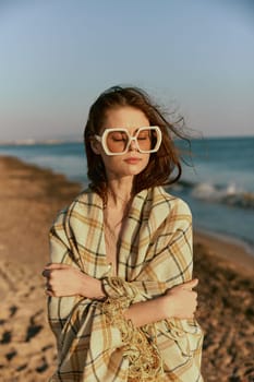 portrait of a woman in massive glasses wrapped in a plaid enjoying a warm day at the sea, facing the camera. High quality photo