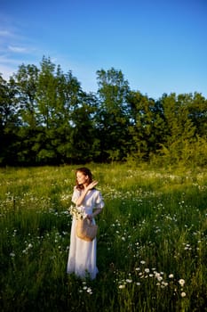 a beautiful woman stands in a flowering field on a sunny day in a light summer dress and with a wicker basket full of flowers. High quality photo
