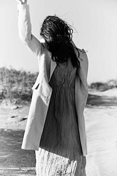 monochrome photo of a woman in a jacket against a clear sky on the coast posing with her hand raised up. High quality photo