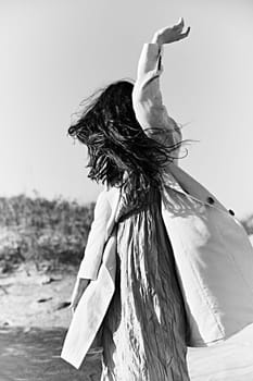 monochrome photo of a woman in a jacket against a clear sky on the coast posing with her hand raised up. High quality photo