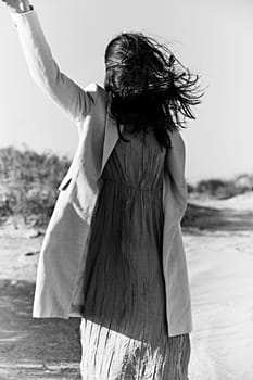 monochrome photo of a woman in a jacket against a clear sky on the coast posing with her hand raised up. High quality photo