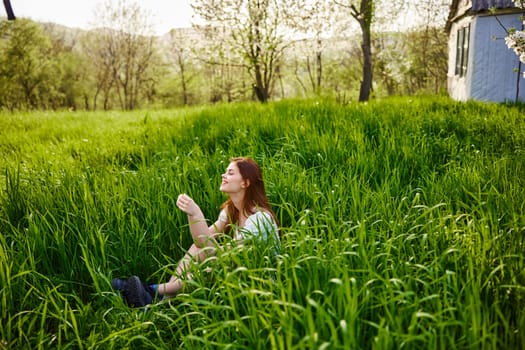 cheerful woman sitting in tall grass near small house in countryside. High quality photo