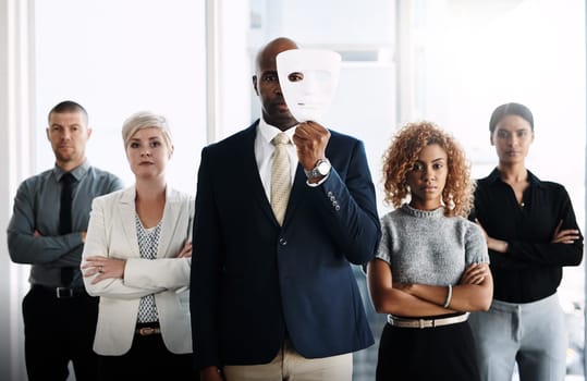 Unmasking business. Portrait of a businessman holding a mask in front of his face with his colleagues standing alongside him in an office