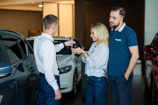 The seller hands over the car keys to the buyers. The couple bought a new car