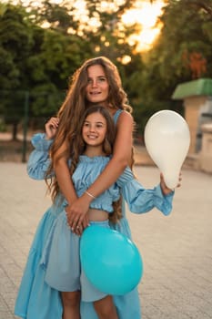 Mother daughter sunset. in blue dresses with flowing long hair against the backdrop of sunset. The woman hugs and presses the girl to her. They are looking at the camera