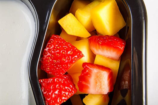 Portion of yogurt dessert with strawberry and mango in a plastic cup. High quality photo. Close-up.